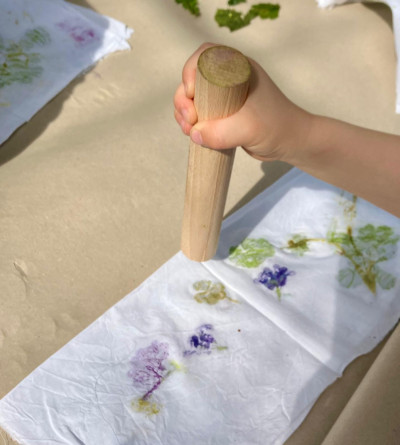 Kind drückt mit einem Holzstempel farbige Blüten auf weißem Stoff ab