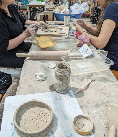 Zwei Personen arbeiten gemeinsam an Keramikprojekten an einem Werkstatttisch mit Ton, Werkzeugen und verschiedenen Keramikformen