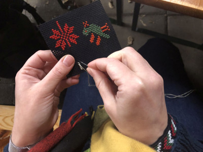 Hände beim Sticken eines blauen Stoffes mit roten und grünen Ornamenten