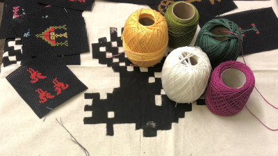 Handgesticktes Kreuzstichprojekt mit Pixelkunst-Motiven und verschiedenfarbige Garnrollen für die Stickerei