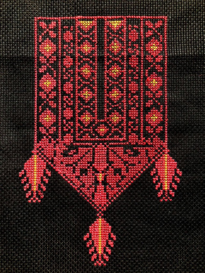 Rotes besicktes Muster mit geometrischen Ornamenten und gelben Akzenten auf schwarzem Stoff, traditionelles Tatreez-Design mit hängenden Verzierungen