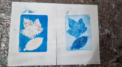 Zwei experimentelle Drucke mit blauen Hintergründen zeigen weiße und blaue Blatt- und Federabdrücke