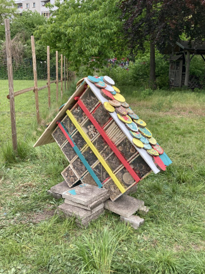 Buntes selbstgebautes Insektenhotel aus recycelten Materialien mit bemaltem Dach in einem Garten
