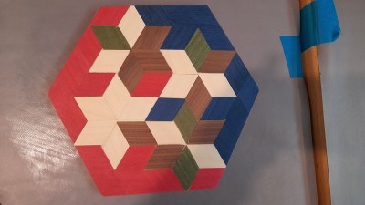 Das fertige Ergebnis eines Marketerie-Workshops. Ein Sechseck aus verschiedenen Holz-Vierecken zusammengesetzt. Die Vierecke haben verschiedene Farben.