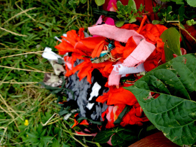 Selbstgebautes Monster aus roten Blüten, schwarzem Papier und rosa Bändern im Gras