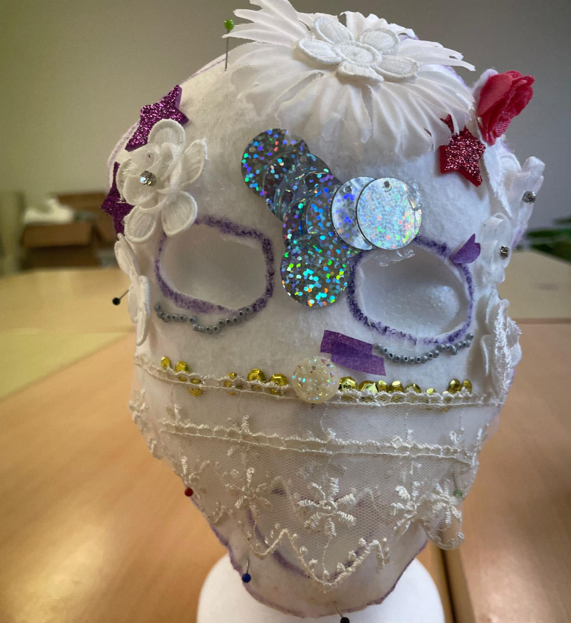 text: >
  Eine selbst gestaltete Maske auf einem
  Frisierkopf. Die Maske besteht aus
  weißem Tüll mit vielen einzelnen
  glitzernden Deko-Elementen. Die Augen
  sind ausgeschnitten.
decorative: false
source: manual
