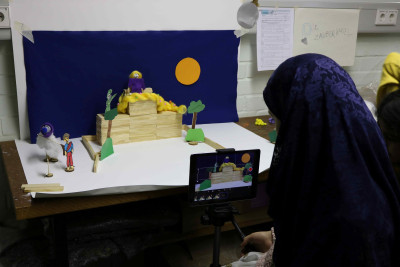 Schülerin filmt mit einem Tablet ein selbstgebautes Diorama aus Holzblöcken, Figuren und Kulissen für ein Trickfilmprojekt
