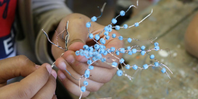 Hände halten ein kunstvolles Drahtbäumchen mit blauen Perlen