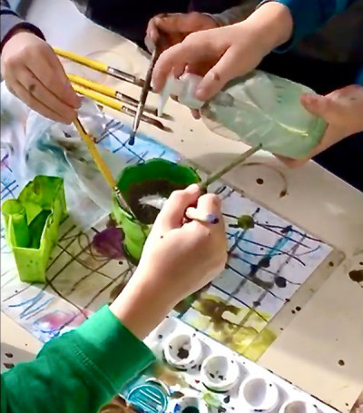 Kinder malen gemeinsam mit Pinseln und Wasserfarben an einem mit Papier bedeckten Tisch