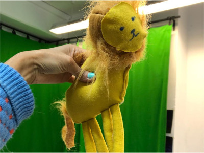 „Handpuppe in Form eines gelben Löwen vor einem grünen Hintergrund.“