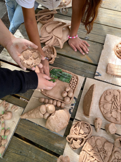 Mehrere Hände von Kindern formen und gestalten Kunstwerke aus Ton auf Holztischen