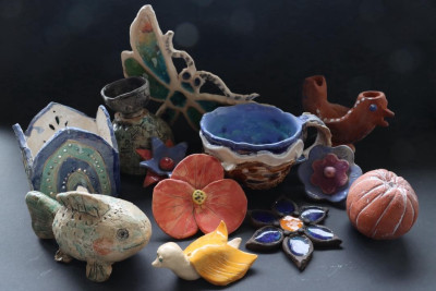 Sammlung handgetöpferter Keramikobjekte mit bunten Schalen, Tierfiguren und Kürbissen auf dunklem Untergrund