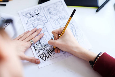 „Person zeichnet mit einem Bleistift Comicfiguren in einem Skizzenbuch.“