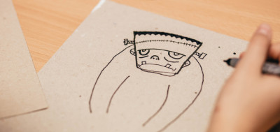 Kind zeichnet Comicfigur mit Frankenstein-Monster auf Papier