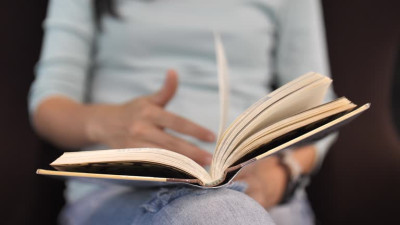 „Person hält ein aufgeschlagenes Buch auf dem Schoß.“