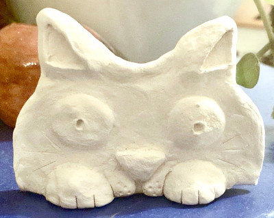 Weißes Gipsrelief in Form einer liegenden Katze mit ausgeprägten Pfoten und Gesichtszügen
