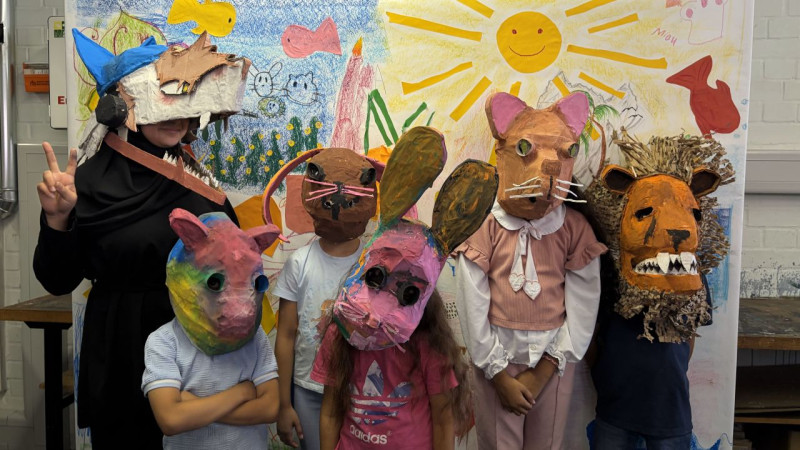 text: >
  Fünf Kinder mit selbstgebastelten
  Tiermasken posieren vor einer bunten
  Wandmalerei mit Sonne, Vögeln und
  Pflanzen
decorative: false
source: reviewed