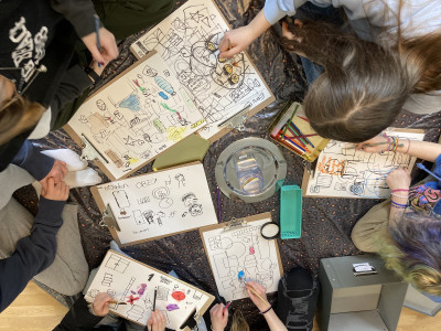 „Kinder zeichnen gemeinsam mit Buntstiften auf Papier.“