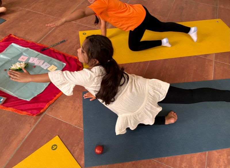 text: >
  Zwei Kinder üben Yoga auf blauen und
  gelben Matten und halten eine
  Balancepose, während neben ihnen ein
  kleines Tuch mit Karten und einer Blüte
  liegt.
decorative: false
source: manual