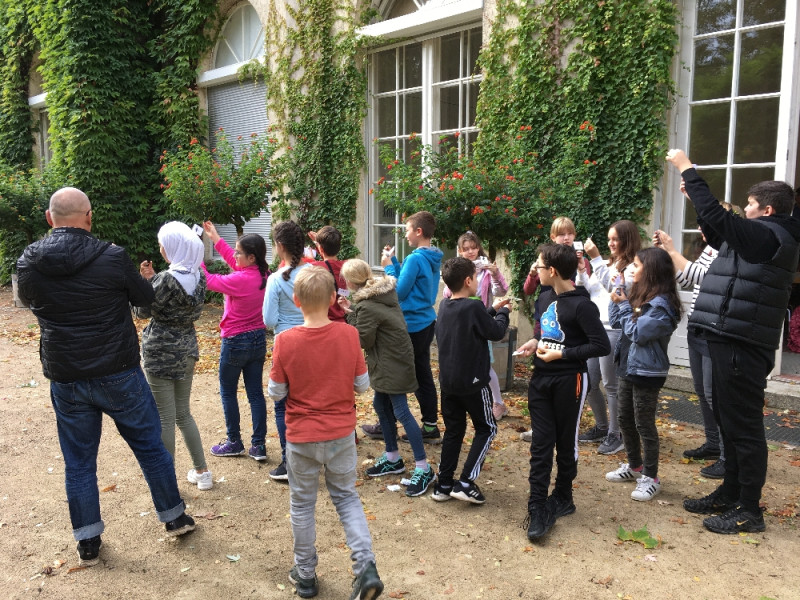 text: >
  Eine Gruppe von Kindern steht mit einer
  erwachsenen Person vor einem mit Efeu
  bewachsenen Gebäude. Viele halten
  kleine weiße Gegenstände hoch
decorative: false
source: manual