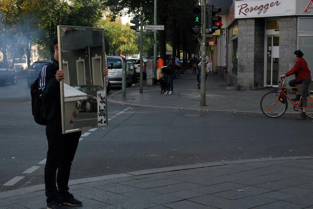 Ein junger Mensch hält einen Spiegel an einer Straßenecke