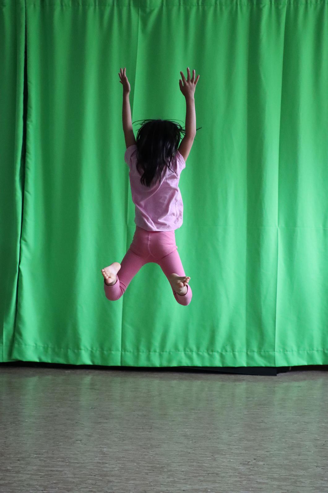 Ein Kind macht einen Luftsprung vor einem grünen Vorhang